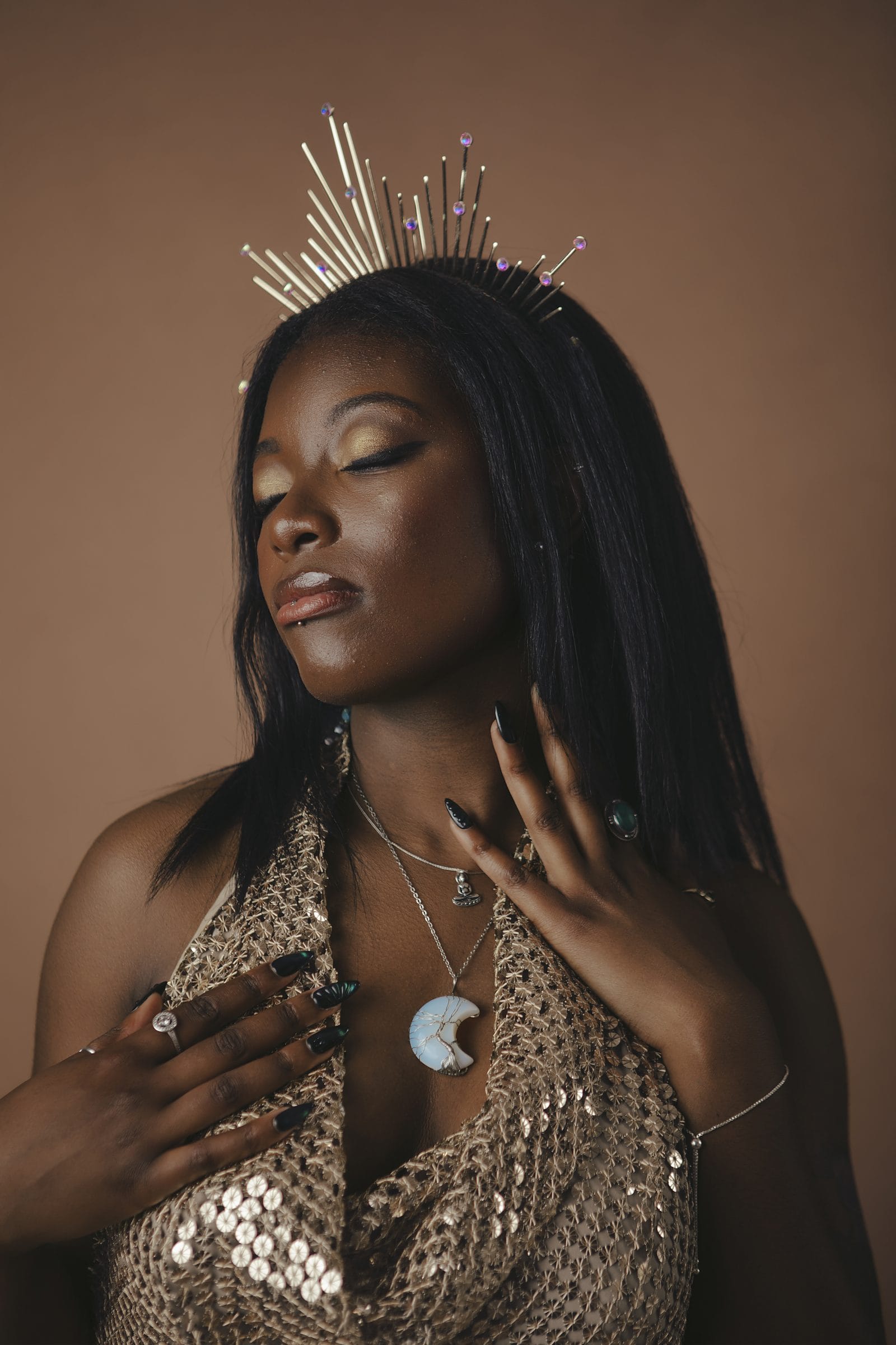 Woman in gold sequins and a delicate crown, hand to her chest, a glamorous portrait at Body & Soul Studios, London.