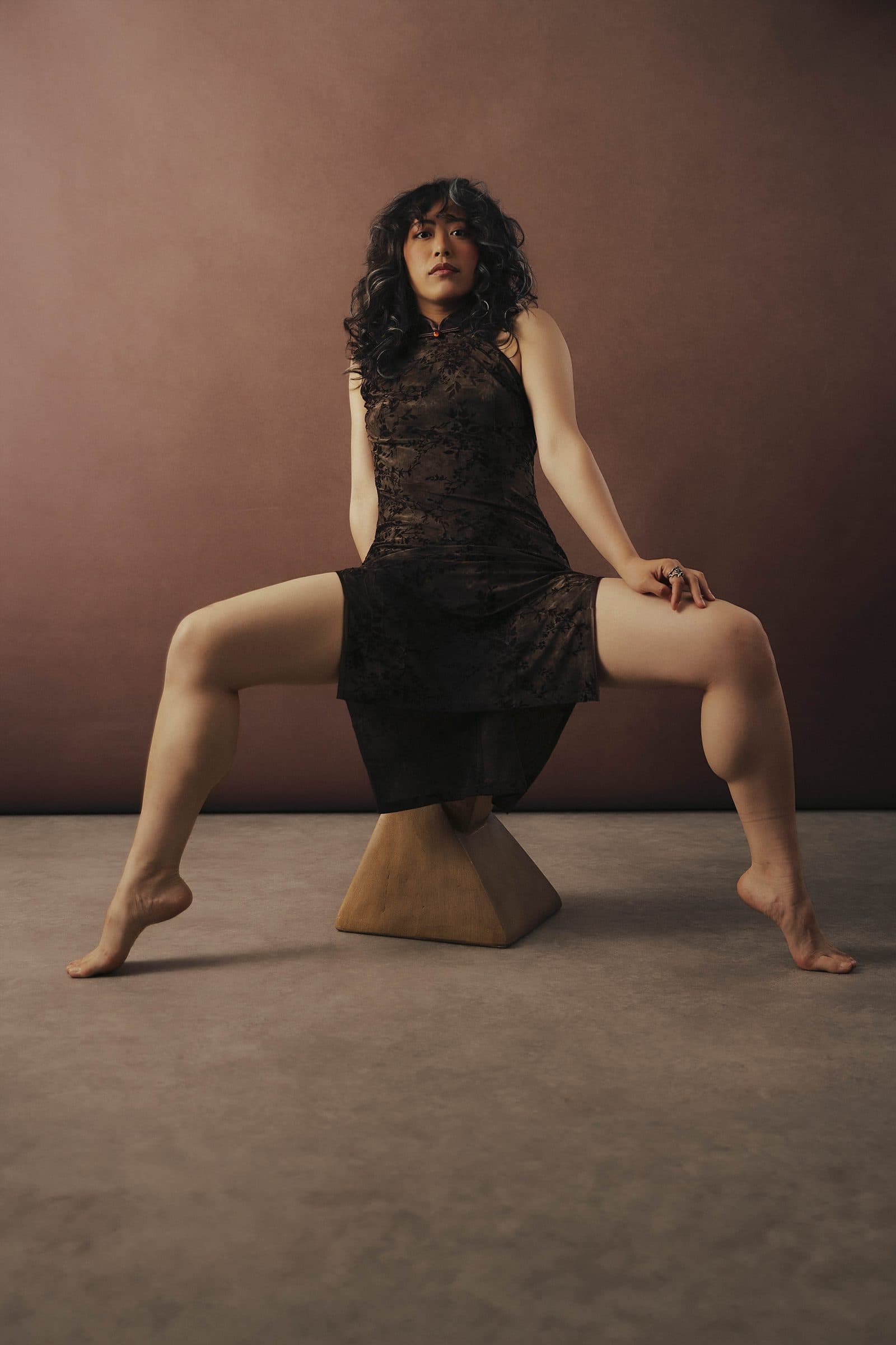 Woman in a black dress seated on a sculptural pedestal, poised and striking, at Body & Soul Studios, London.