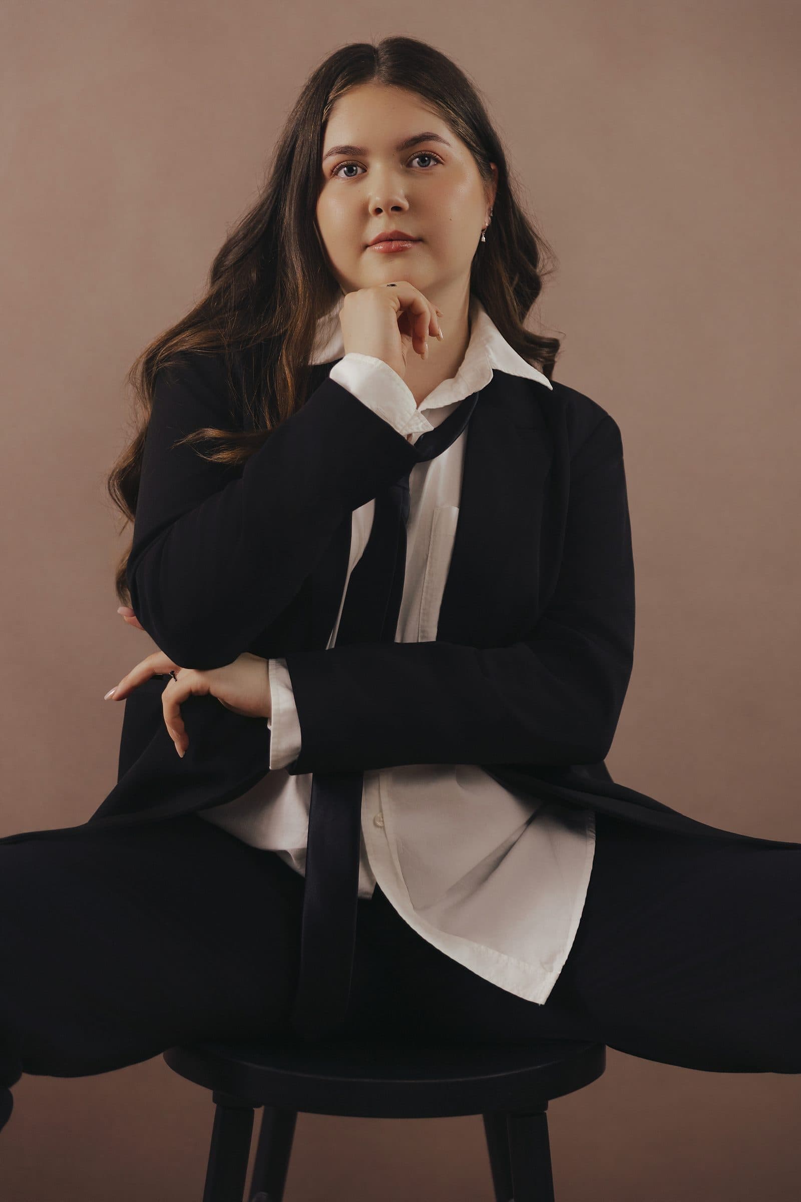 Woman in a sharp black suit with white cuffs, long hair, seated and composed, at Body & Soul Studios, London.