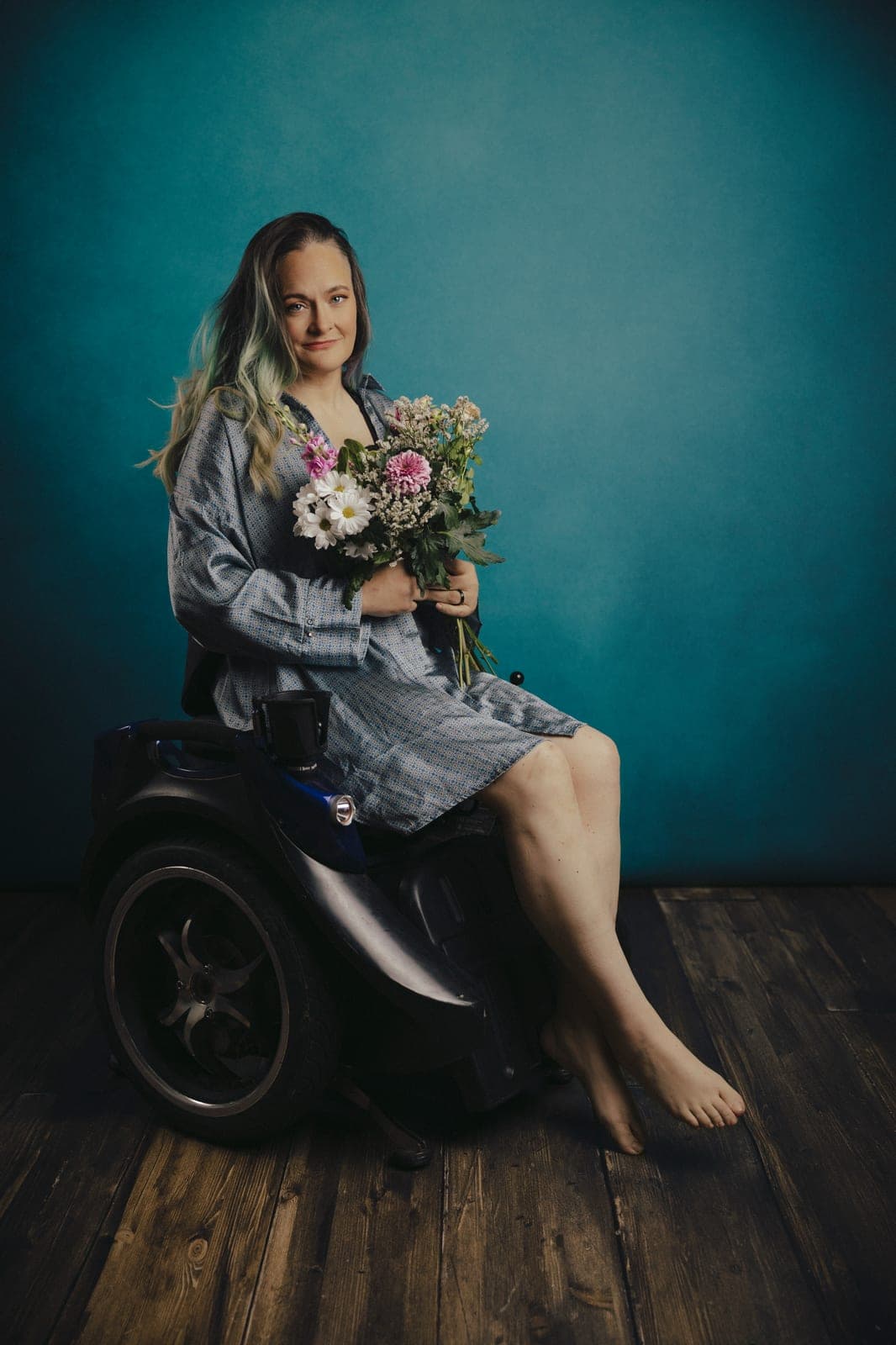 Woman seated in her wheelchair holding a bouquet of wildflowers, serene and radiant, at Body & Soul Studios.