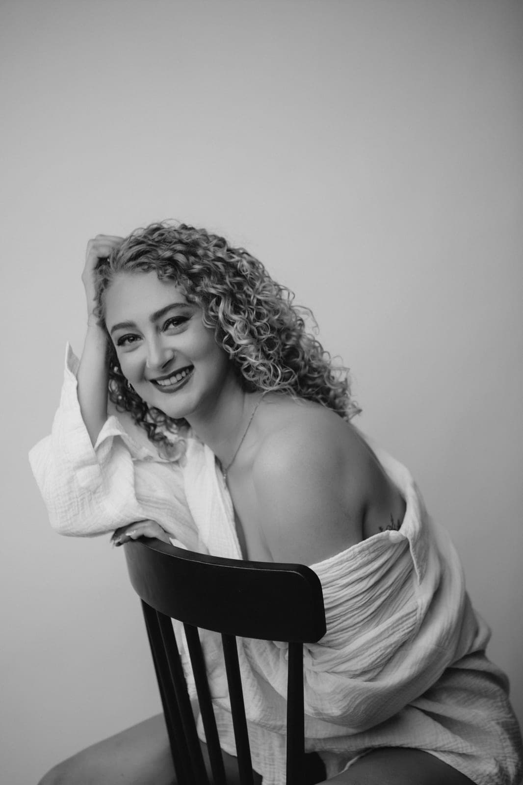 Woman with curly hair laughing freely in an off-shoulder shirt, a joyful black-and-white portrait at Body & Soul Studios, London.