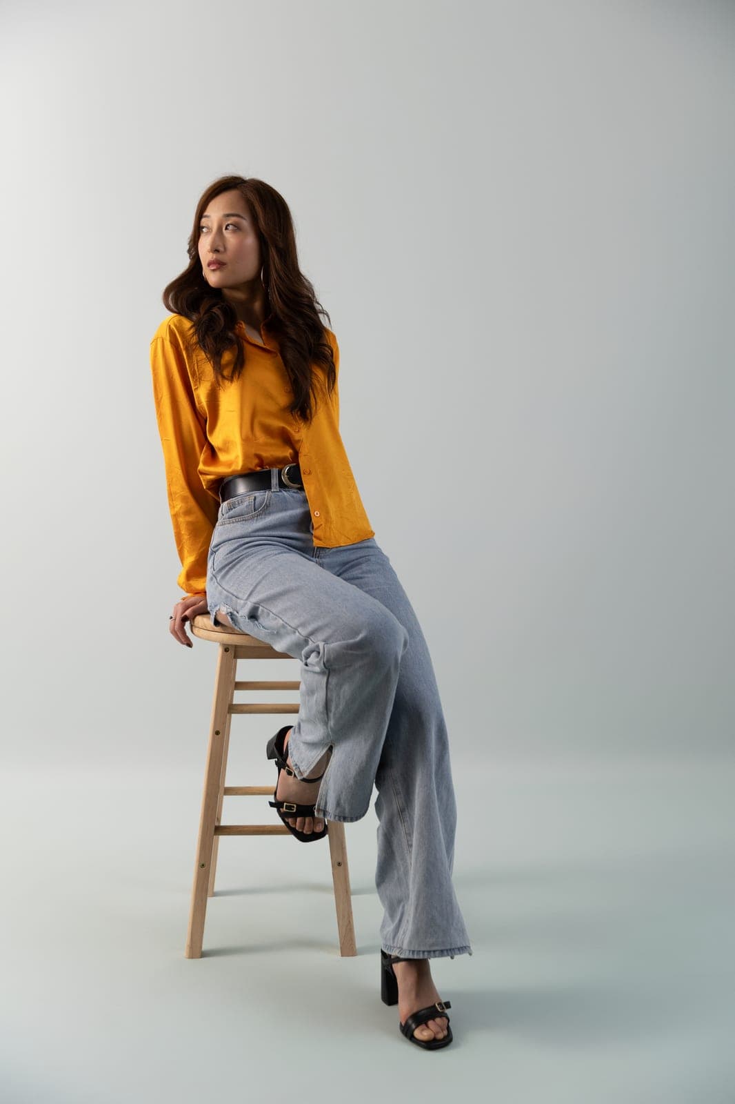 Woman in an orange satin shirt and wide-leg jeans on a studio stool, relaxed and editorial, at Body & Soul Studios.